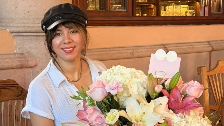 Alexa sonriendo detrás de un ramo de flores